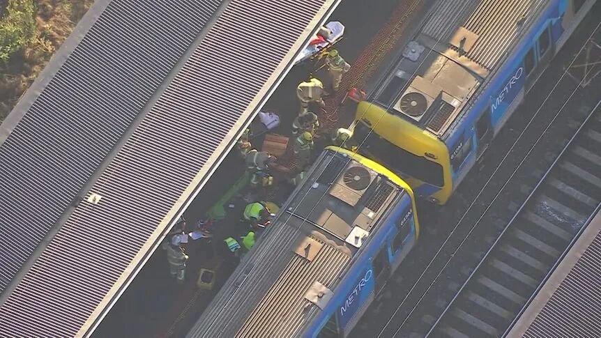An aerial shot of emergency service workers in uniforms and helmets standing on a platform beside two train carriages.
