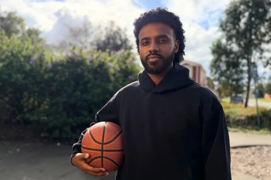 A young man holding a basketball looks at the camera.