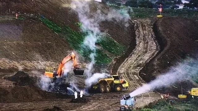 Smoke rising from the ground at a tip with trucks working on the site nearby.