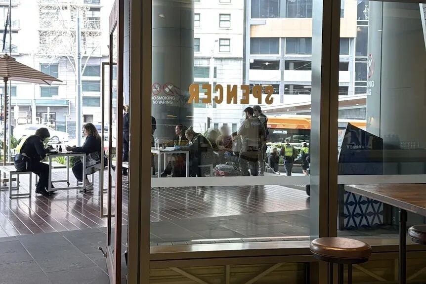 A photo taken from inside a cafe looking through the glass doors to police standing near a boy and woman.